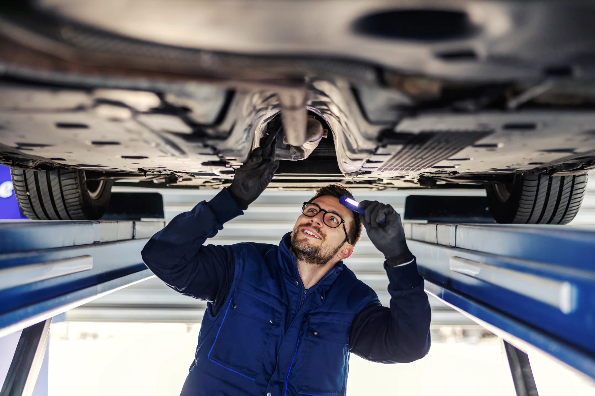 Photo réaliste professionnelle d’un centre de contrôle technique automobile moderne, avec une voiture légère positionnée sur une ligne d’inspection dans un atelier propre et lumineux, un contrôleur en tenue de travail vérifiant le véhicule à proximité de la fosse de contrôle et des équipements de mesure, ambiance sérieuse, sécurisée et accueillante.